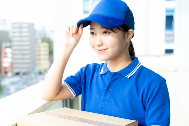 アニメグッズの入った段ボールを持った配送業の女性
