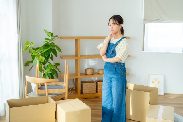 引越し後の荷ほどきでグッズの段ボールを置くスペースが足りずに悩む女性